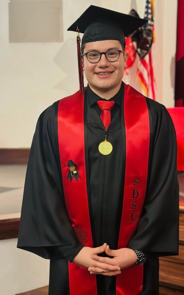 Joel, RN and founder of 4NURS, smiling in his graduation cap and gown